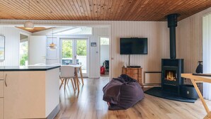 Ein modernes Interieur mit Holzbalkendecke, einer Küchenzeile, einem Wohnzimmer mit Kamin und einem an der Wand montierten Fernseher.