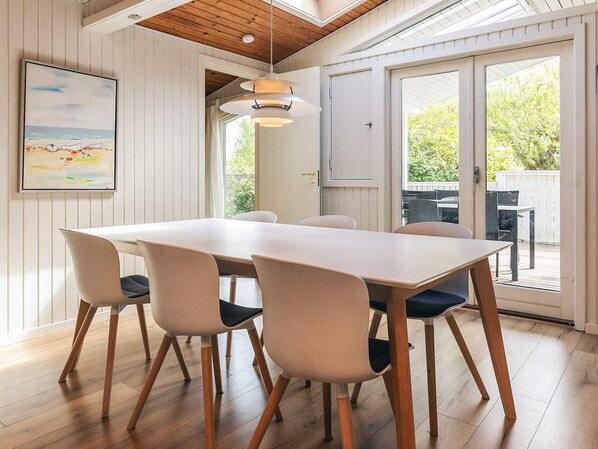 A dining area with a white table and chairs, a pendant light, and a view of the outdoors through a glass door.