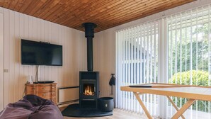 Ein gemütlicher Raum mit Holzbalkendecke, einem an der Wand befestigten Fernseher, einem Kamin, einem Sofa und einem Tisch.
