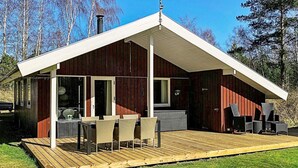 A modern cabin with a covered deck, large windows, and outdoor seating. - Cozy Holiday Home in Læsø near Sea (Læsø)