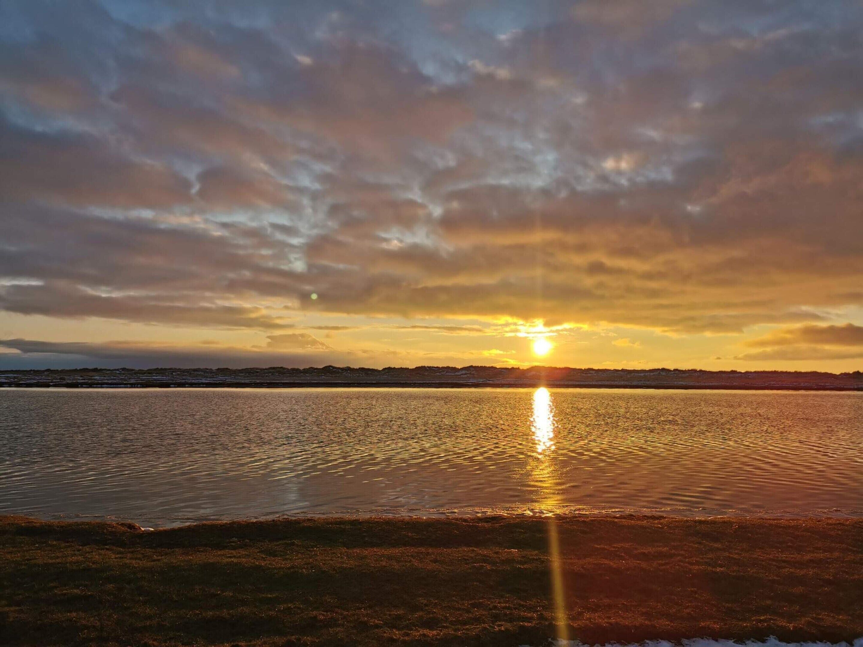 A sunset over a calm body of water with a distant shoreline.