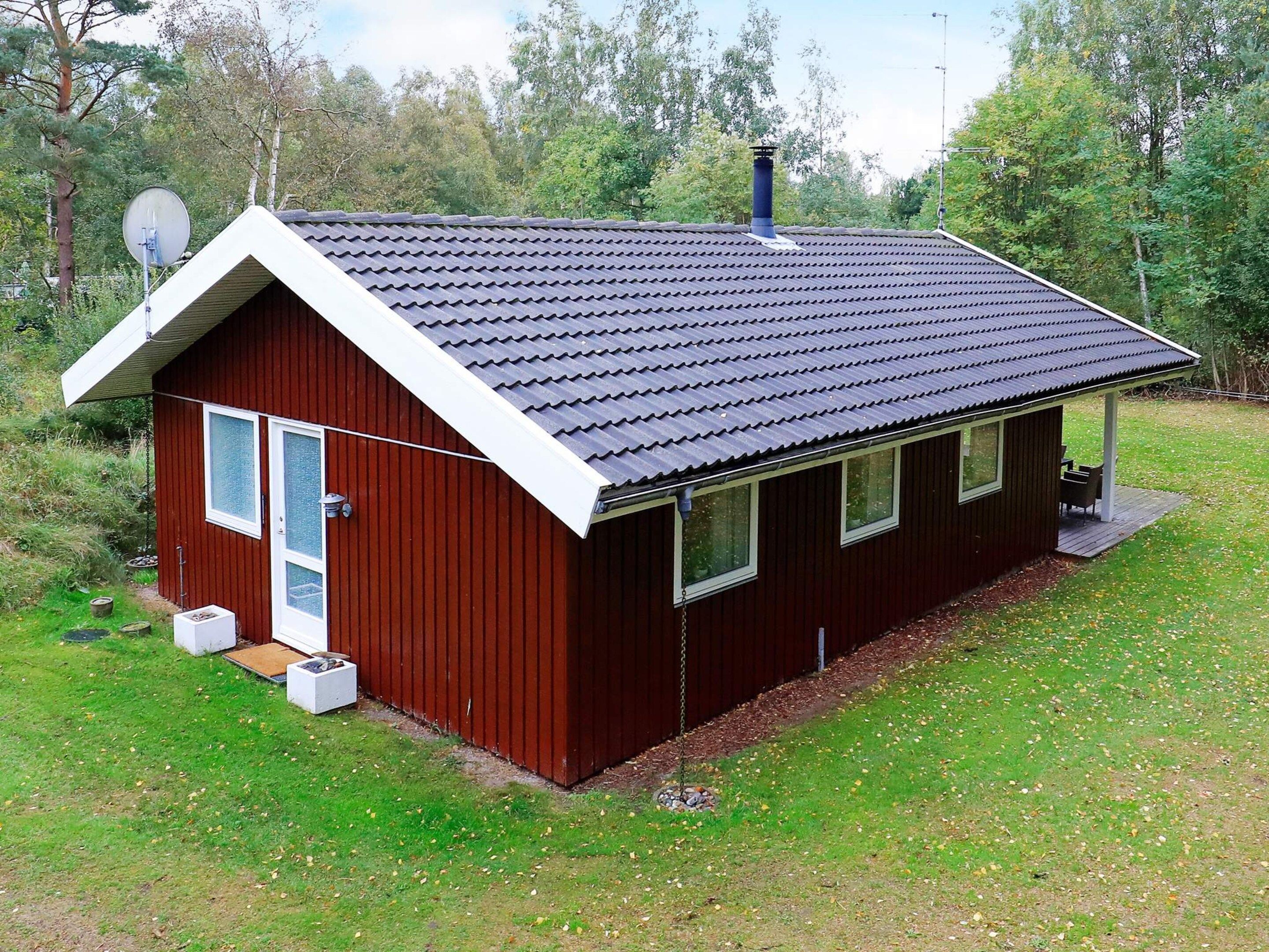 A small, single-story wooden cabin with a dark roof, a porch with seating, and a satellite dish on the roof.