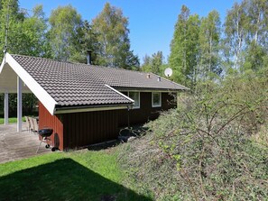 A single-story wooden cabin with a tiled roof, a satellite dish, and a small deck area.