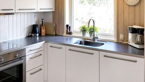 A modern kitchen with white cabinets, a stainless steel sink, and a built-in oven. - Cozy Holiday Home in Læsø near Sea (Læsø)
