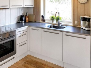 A modern kitchen with white cabinets, a stainless steel range, a sink, and a window with a view of greenery.