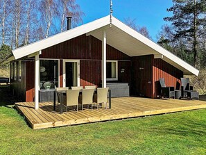 Eine moderne Holzhütte mit überdachter Terrasse, Sitzgelegenheiten im Freien und einem Schornstein.