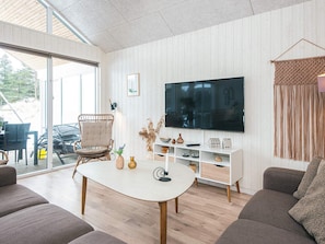 A modern living room with a large TV, comfortable seating, and a glass door leading outside.