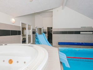 A swimming pool with a hot tub, a slide, and a door leading to a changing room.