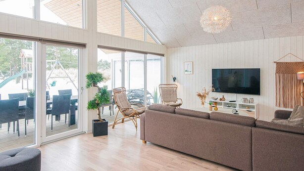 A spacious living room with a large sectional sofa, a television, and a dining area with outdoor seating. - 5 Star Holiday Home in Blavand (Blavand)