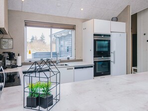 A modern kitchen with a built-in oven, a dishwasher, and a window with a view of a house.
