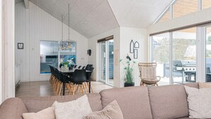 A modern living room with a large beige sofa, a dining area with a long table and chairs, and a view of the outdoors through large windows. - 5 Star Holiday Home in Blavand (Blavand)