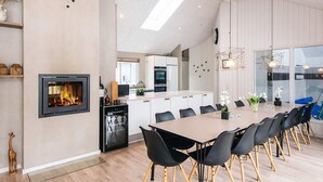 A modern kitchen with a central island, a dining area with a long table and chairs, and a fireplace. - 5 Star Holiday Home in Blavand (Blavand)