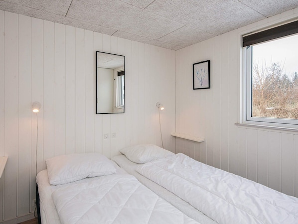 A single bed with white bedding in a room with white walls and a window.