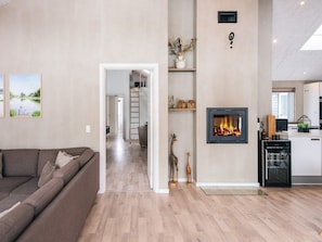 A modern living room with a sofa, a fireplace, and a kitchen area visible through an open door.