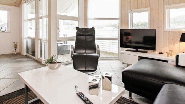 A modern living room with a large window, a television, a black leather chair, a white table, and a black sofa. - 6 Person Holiday Home in Ansager-by Traum (Ansager)