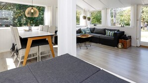 A spacious living area with a dining table and sofa, large windows, and a hanging light fixture. - Tranquil Retreat in Blavand - By Traum Ferienwohnungen (Blavand)