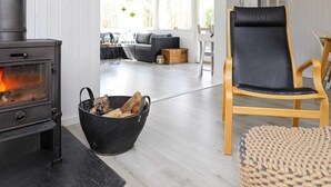 A cozy living room with a wood-burning stove, a black chair, and a view of the outdoor seating area. - Tranquil Retreat in Blavand - By Traum Ferienwohnungen (Blavand)
