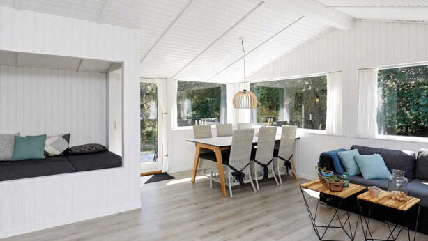 A modern living room with a dining area, white wooden walls, and large windows. - Tranquil Retreat in Blavand - By Traum Ferienwohnungen (Blavand)