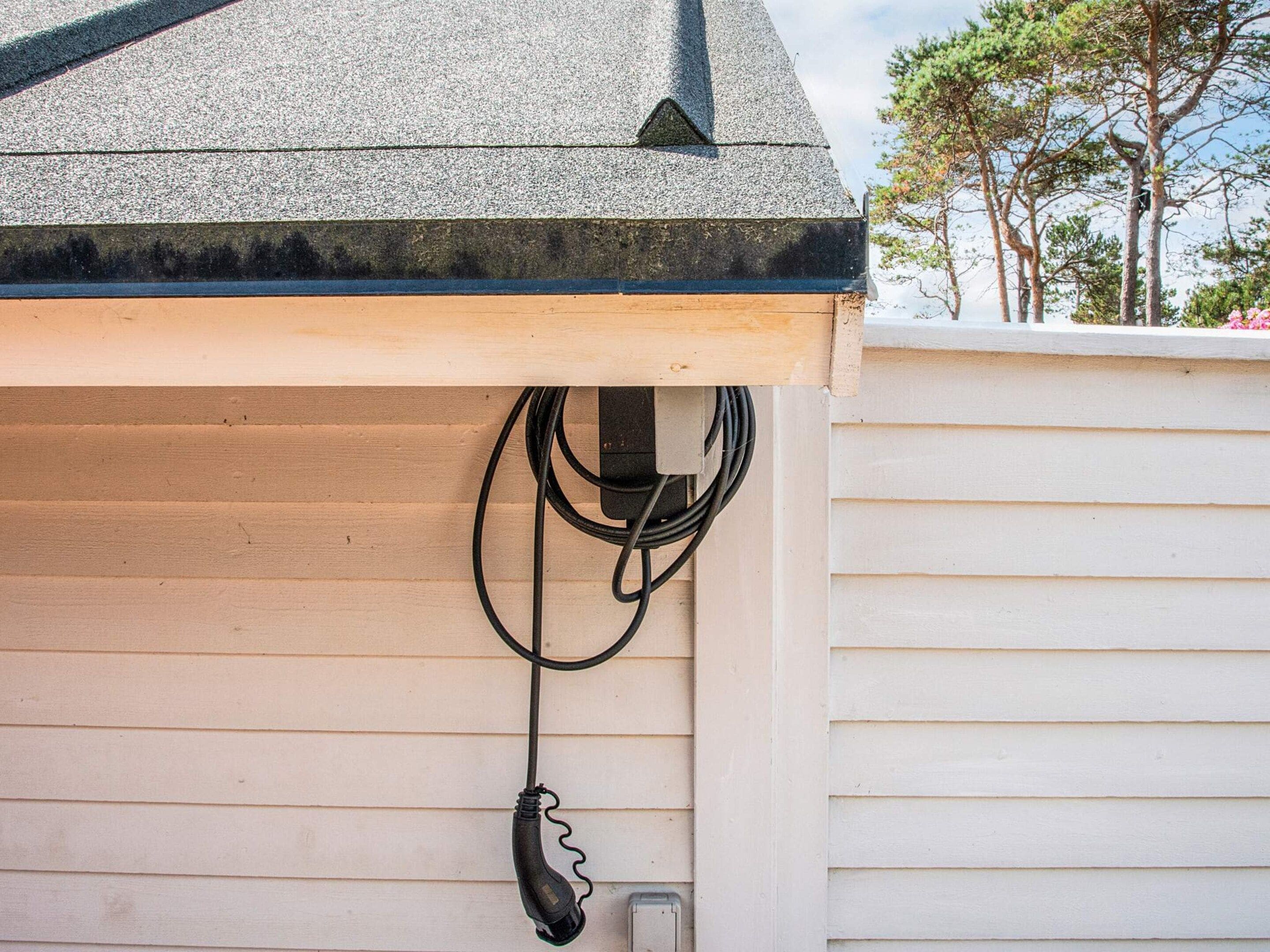 A house with a grey roof, wooden siding, and a black electrical cord hanging from the roof.