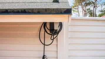 A house with a grey roof, wooden siding, and a black electrical cord hanging from the roof.