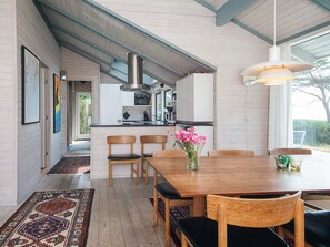 Une cuisine moderne avec un îlot central, des chaises en bois, une table à manger agrémentée d’un vase de fleurs et un luminaire suspendu.
