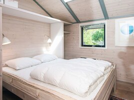 A bed with white bedding in a room with wooden walls and a window with a view of greenery.
