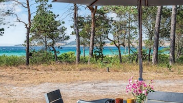 Un espace extérieur aménagé avec une table et des chaises, un vase de fleurs, et une vue sur la mer et les arbres.