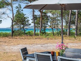 An outdoor seating area with a table and chairs, a flower vase, and a view of the sea and trees.