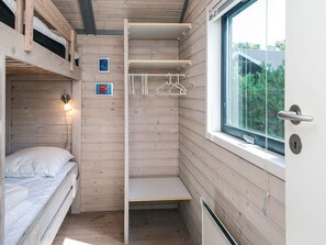 A compact room with a bunk bed, a small shelf, and a window with a view of greenery.