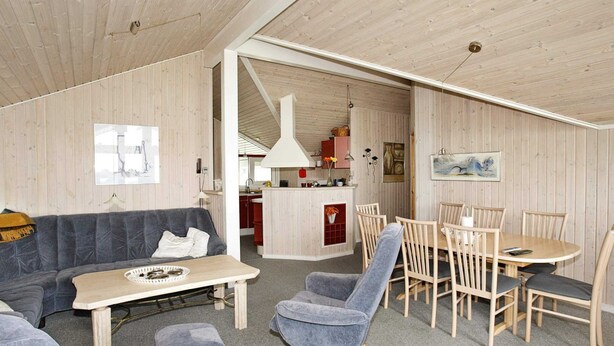 Een modern interieur met een houten plafond, een bank, een eettafel met stoelen en een keukenhoek.