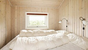 Een slaapkamer met houten plafond, een raam met uitzicht, een bed met wit beddengoed en een bedlampje.