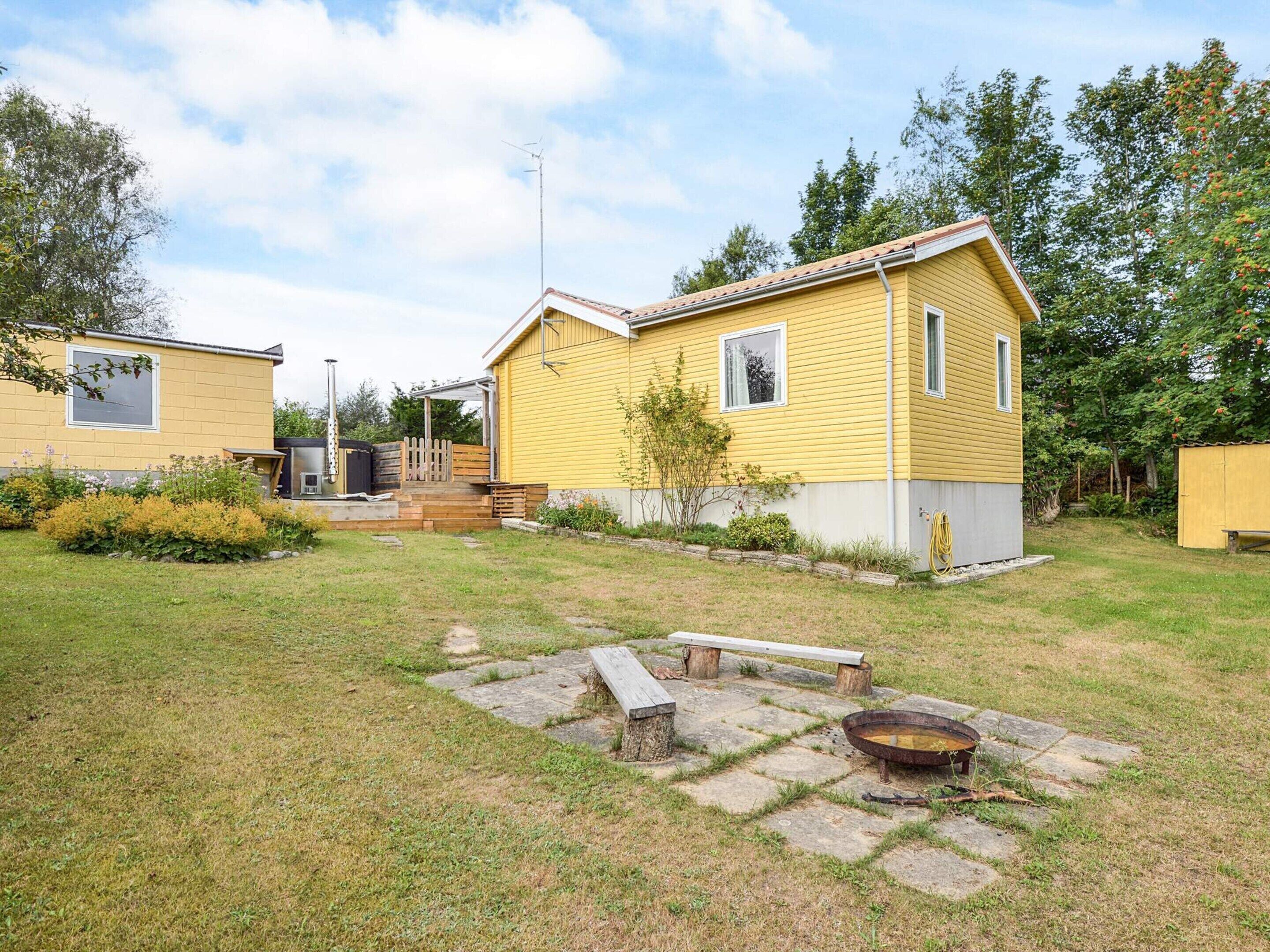 Una casa amarilla con un patio, una fogata y un banco de madera.