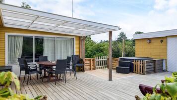 Una terraza techada al aire libre con mesa y sillas, un jacuzzi y una valla de madera.