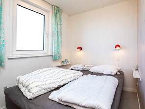 A bedroom with two beds, a window with curtains, and two wall-mounted lamps.