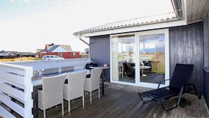 A deck with wicker chairs, a grill, and a glass door leading to a patio. - 4 Star Holiday Home in Lemvig (Lemvig)