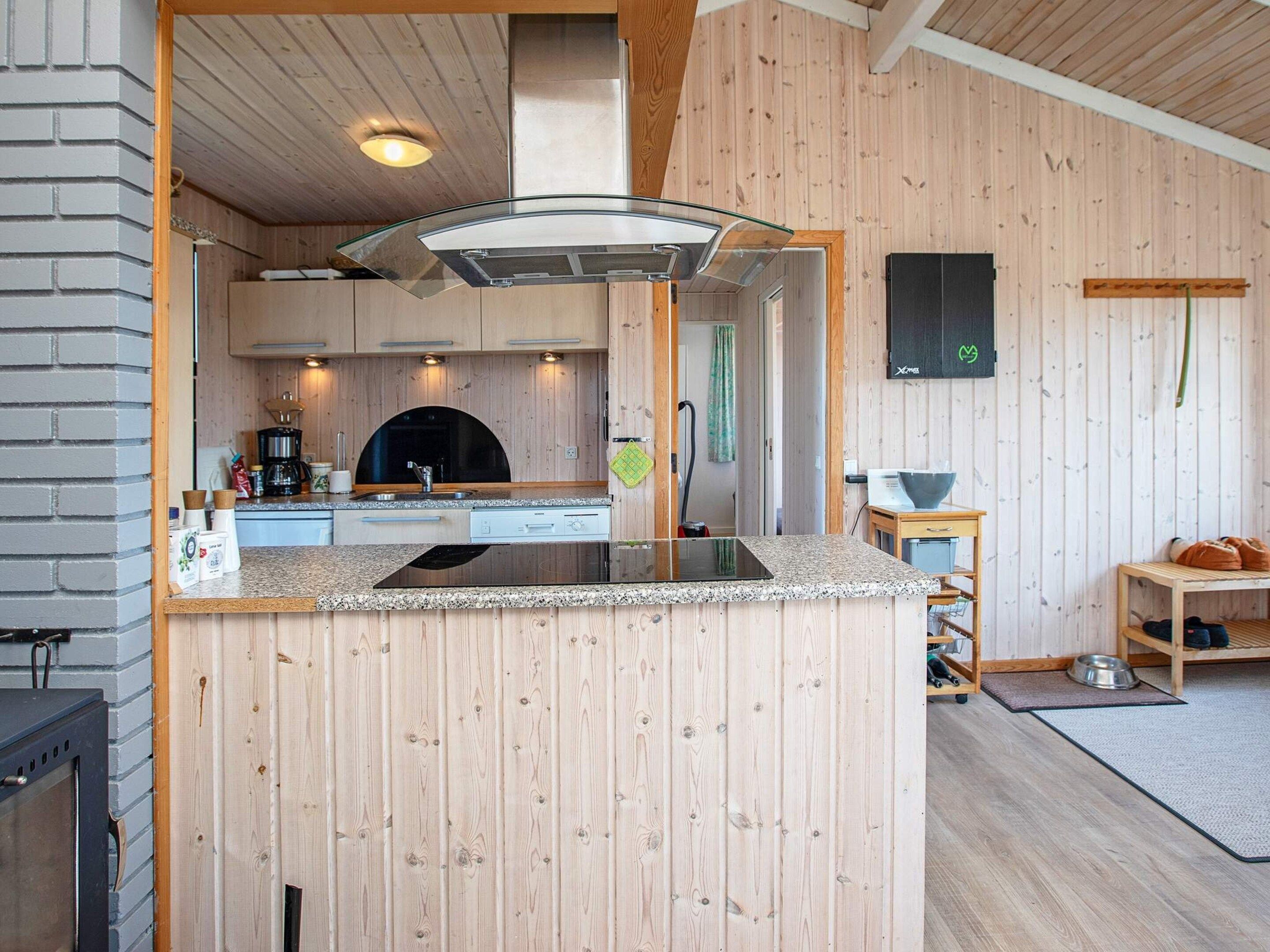 A modern kitchen with a central island, wooden walls, and a built-in stove.