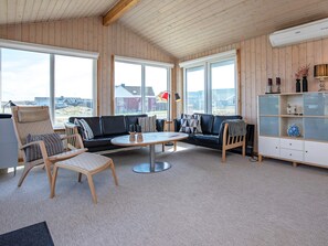 A room with a wooden ceiling, large windows, a black leather sofa, a round coffee table, and a white cabinet with glass doors.