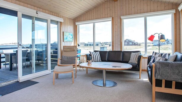 A spacious living area with a large window, a round table, and a sofa. - 4 Star Holiday Home in Lemvig (Lemvig)
