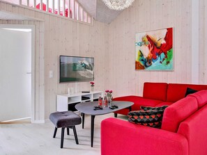 Een moderne woonkamer met een rode bank, een aan de muur bevestigde televisie, en een schilderij erboven.