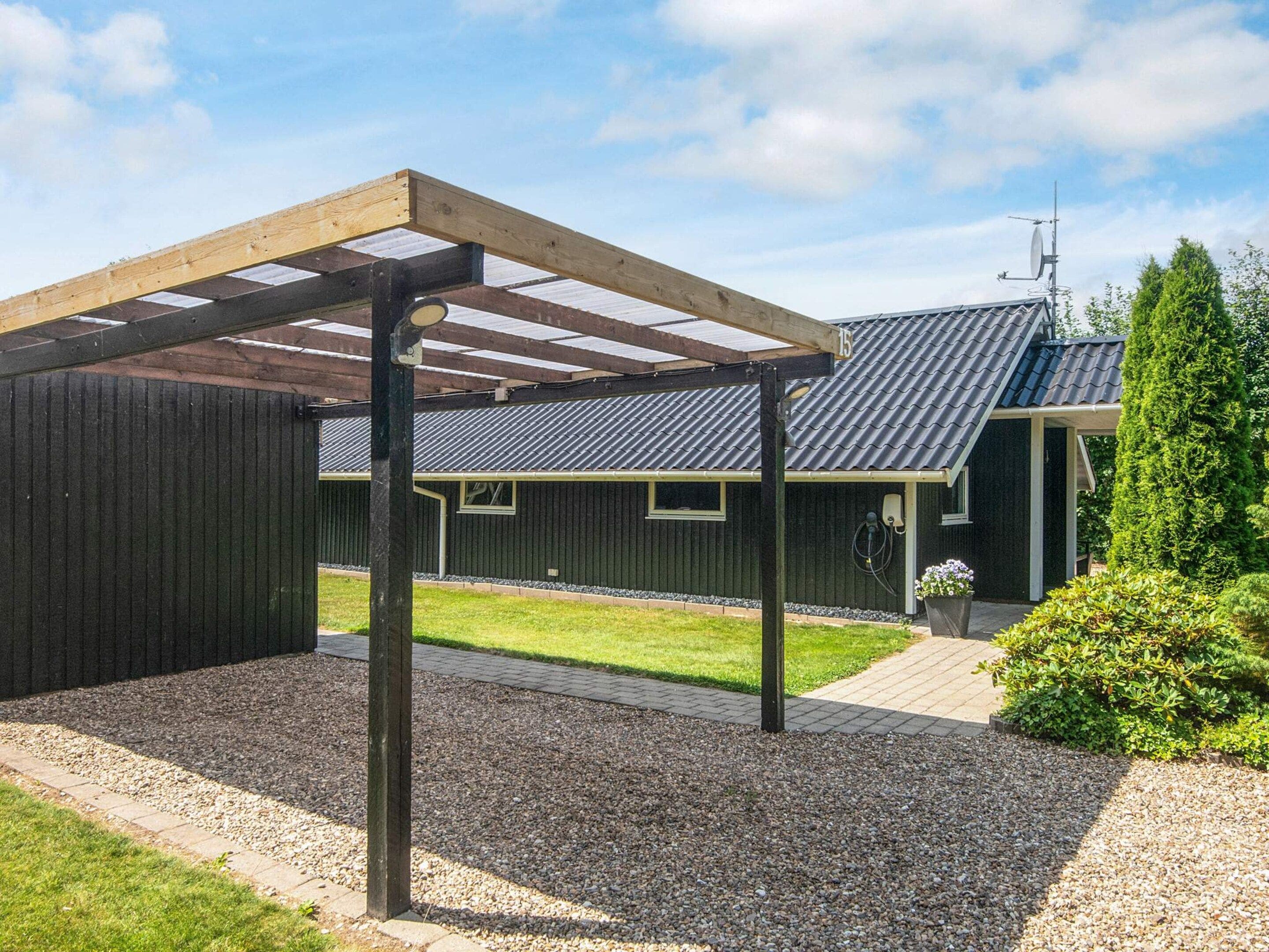 Un espace extérieur abrité, doté d’une pergola en bois, un bâtiment à la façade sombre et une pelouse bien entretenue.