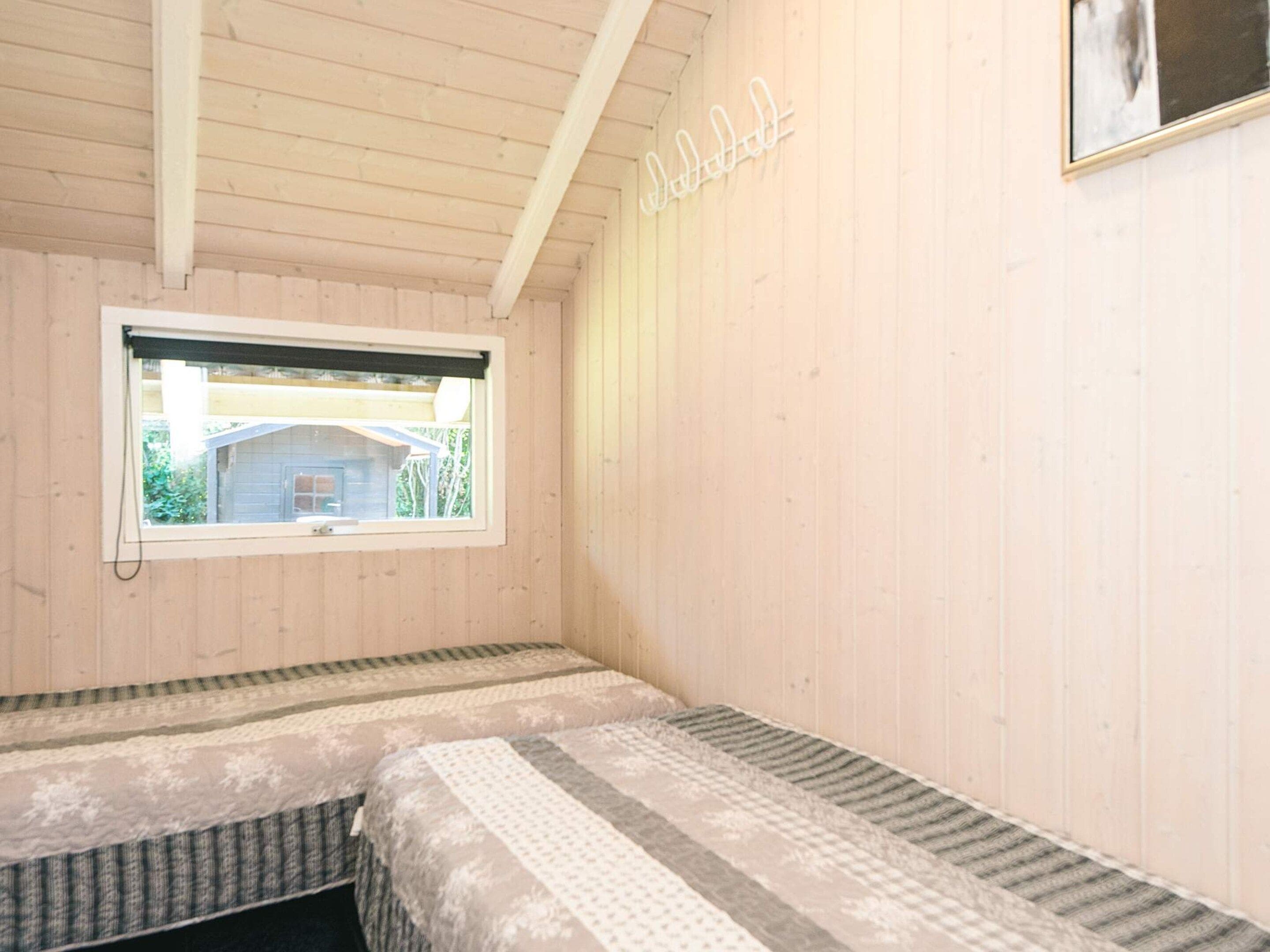Une chambre avec deux lits, une fenêtre donnant sur une maison et un luminaire fixé au mur.