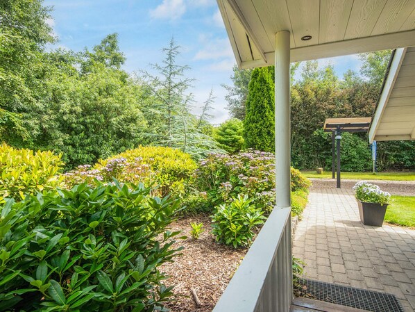 A covered outdoor area with a paved walkway, surrounded by lush greenery and various plants.