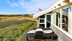 Een terras met lounge fauteuils en een vlag, met uitzicht op een grasland en een gebouw met grote ramen.