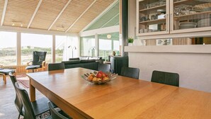 Een ruime eethoek met een houten tafel, stoelen en een schaal fruit. Een groot raam biedt uitzicht op de omgeving.
