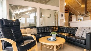 Een moderne woonkamer met een zwarte leren bank, een houten salontafel en een glazen deur naar een balkon.