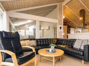 Una sala moderna con un sofá de cuero negro, una mesa de centro de madera y un ventanal que da a un espacio exterior.