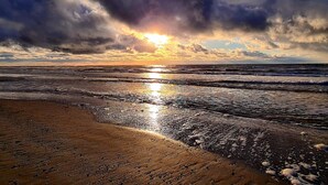 Een strand met golven, een zonsondergang en een bewolkte lucht.