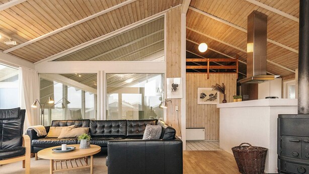 Een ruime woonkamer met een zwarte leren bank, een houten salontafel en een zwart haardvuur.