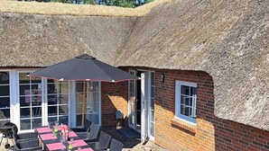 A thatched-roof building with a brick exterior, a covered outdoor dining area with tables and chairs, and a grill. - 5 Star Holiday Home in Vaeggerlose (Vaeggerlose)