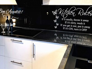 A kitchen with a black countertop, white cabinets, and a decorative sign with kitchen rules.